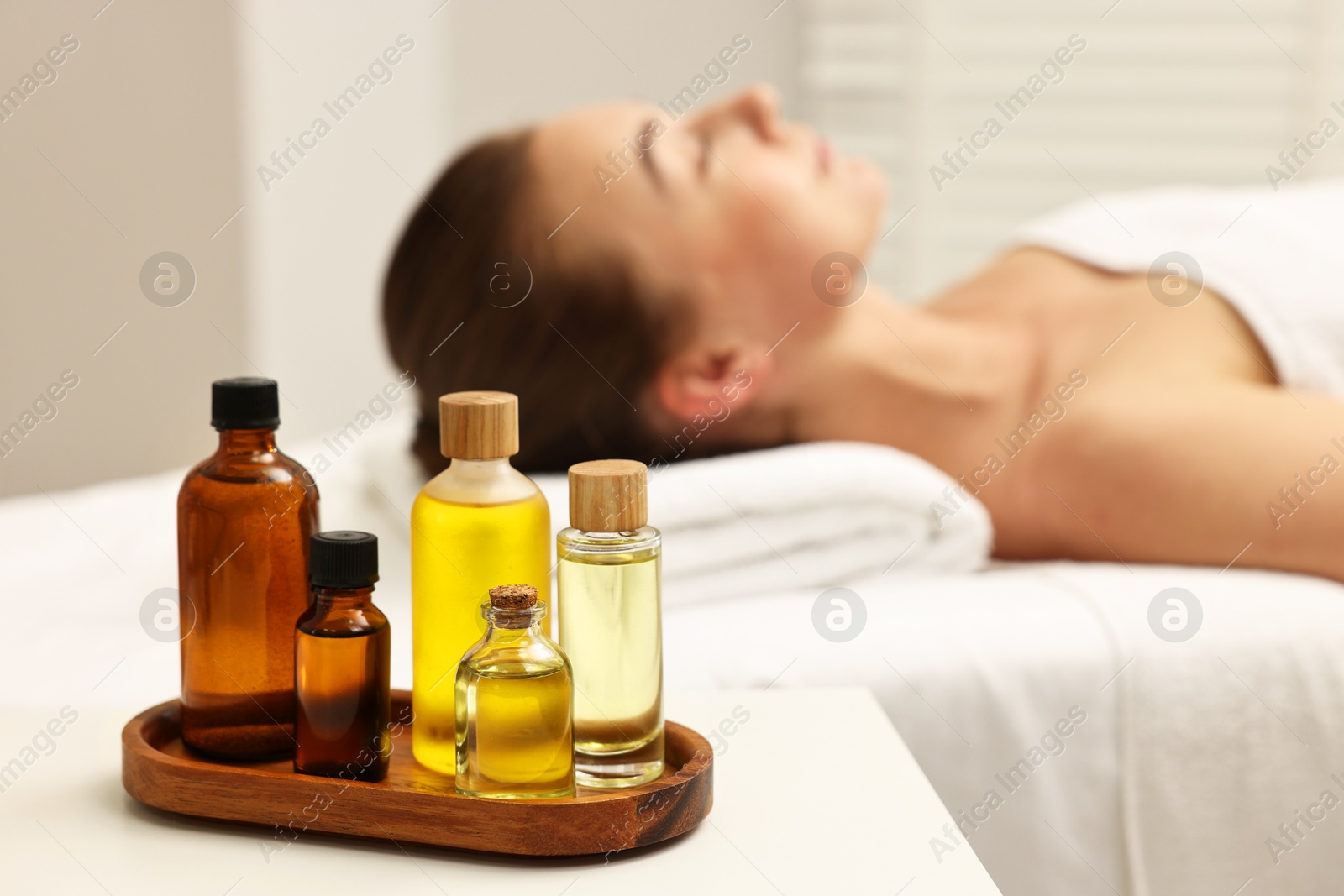 Photo of Aromatherapy. Woman relaxing on massage couch in spa salon, focus on bottles of essential oils