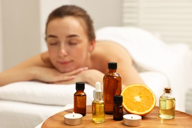 Photo of Aromatherapy. Woman relaxing on massage couch in spa salon, focus on bottles of essential oils, orange and burning candles