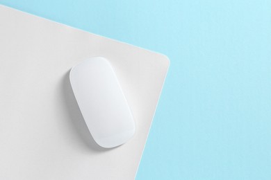 Photo of Wireless mouse and mousepad on light blue background, top view. Space for text