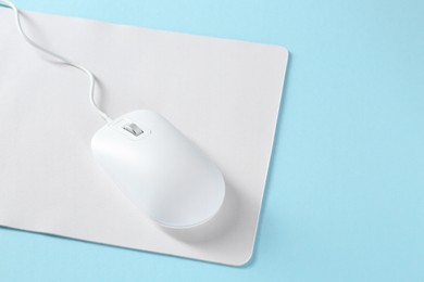 Photo of Wired mouse and mousepad on light blue background, space for text