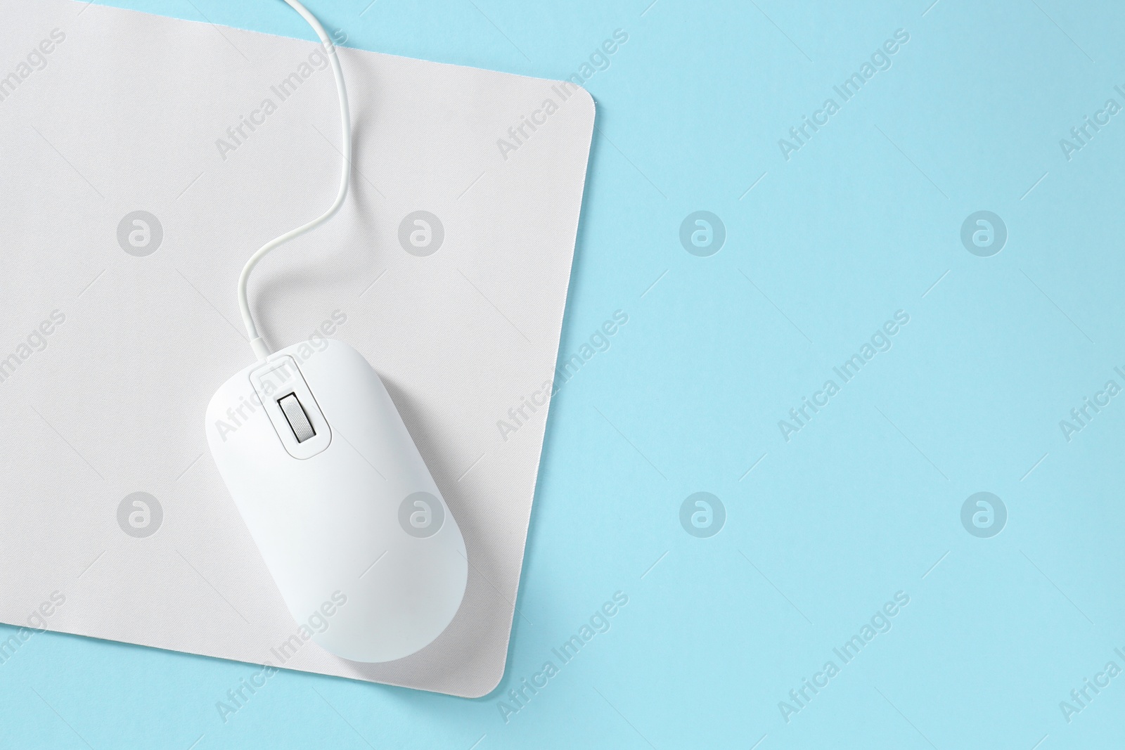 Photo of Wired mouse and mousepad on light blue background, top view. Space for text