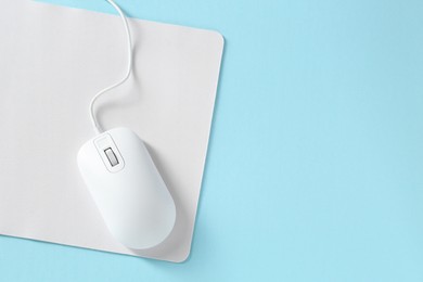 Photo of Wired mouse and mousepad on light blue background, top view. Space for text