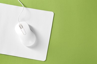 Wired mouse and mousepad on green background, top view. Space for text