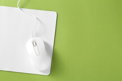 Photo of Wired mouse and mousepad on green background, top view. Space for text