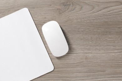 Wireless mouse and mousepad on wooden table, top view. Space for text