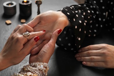 Fortune teller reading lines on woman's palm at black table, closeup. Chiromancy