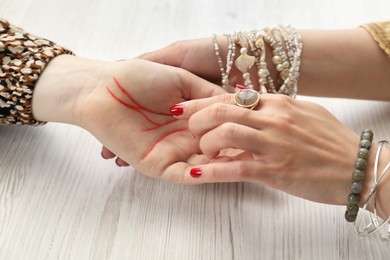 Fortune teller reading lines on woman's palm at white wooden table, closeup. Chiromancy