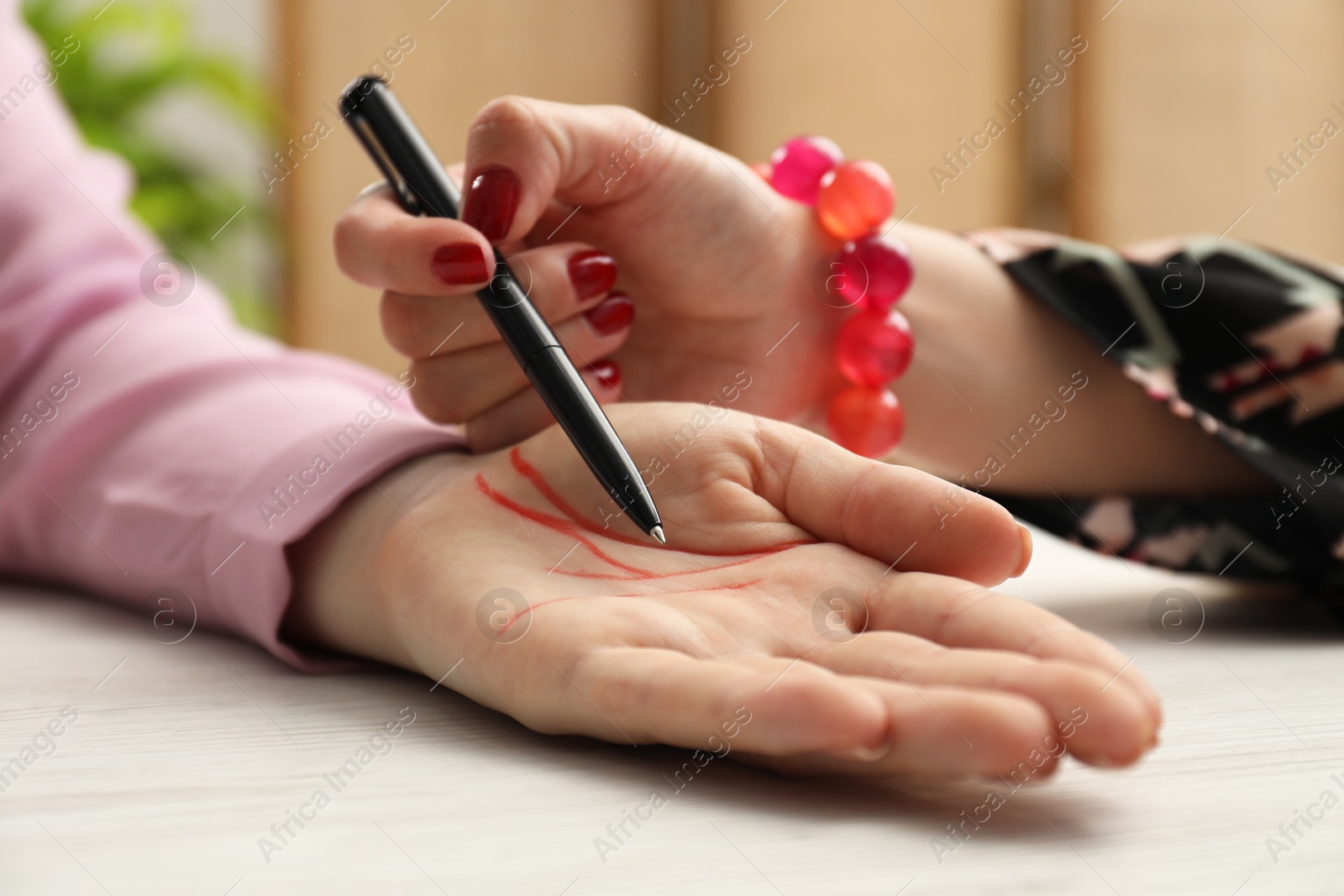 Photo of Fortune teller reading lines on woman's palm at white wooden table, closeup. Chiromancy