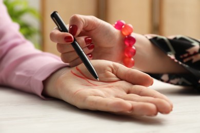 Photo of Fortune teller reading lines on woman's palm at white wooden table, closeup. Chiromancy