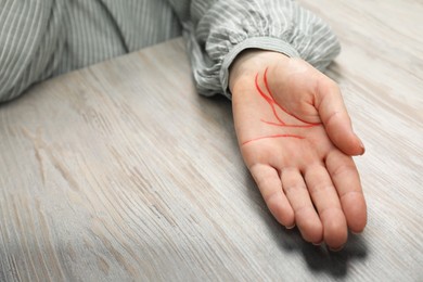 Photo of Chiromancy and foretelling. Woman showing palm with drawn lines at white wooden table, closeup. Space for text