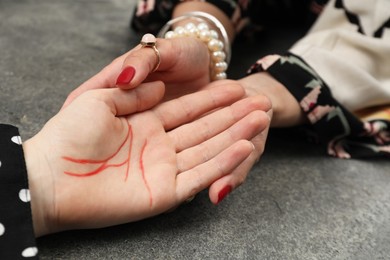 Fortune teller reading lines on woman's palm at grey table, closeup. Chiromancy