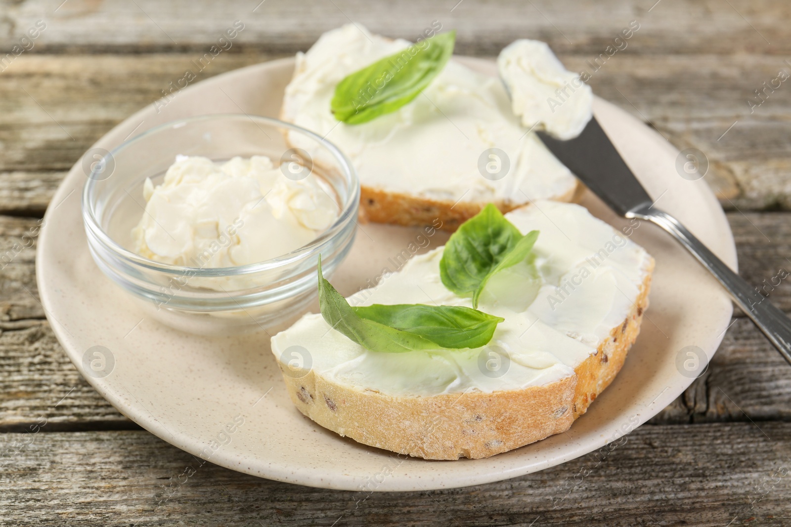 Photo of Delicious sandwiches with cream cheese and basil leaves on wooden table