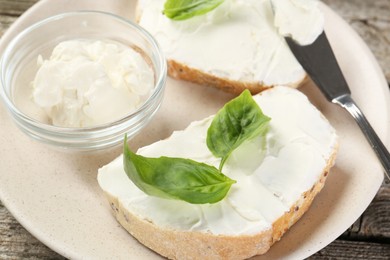 Photo of Delicious sandwiches with cream cheese and basil leaves on wooden table, closeup