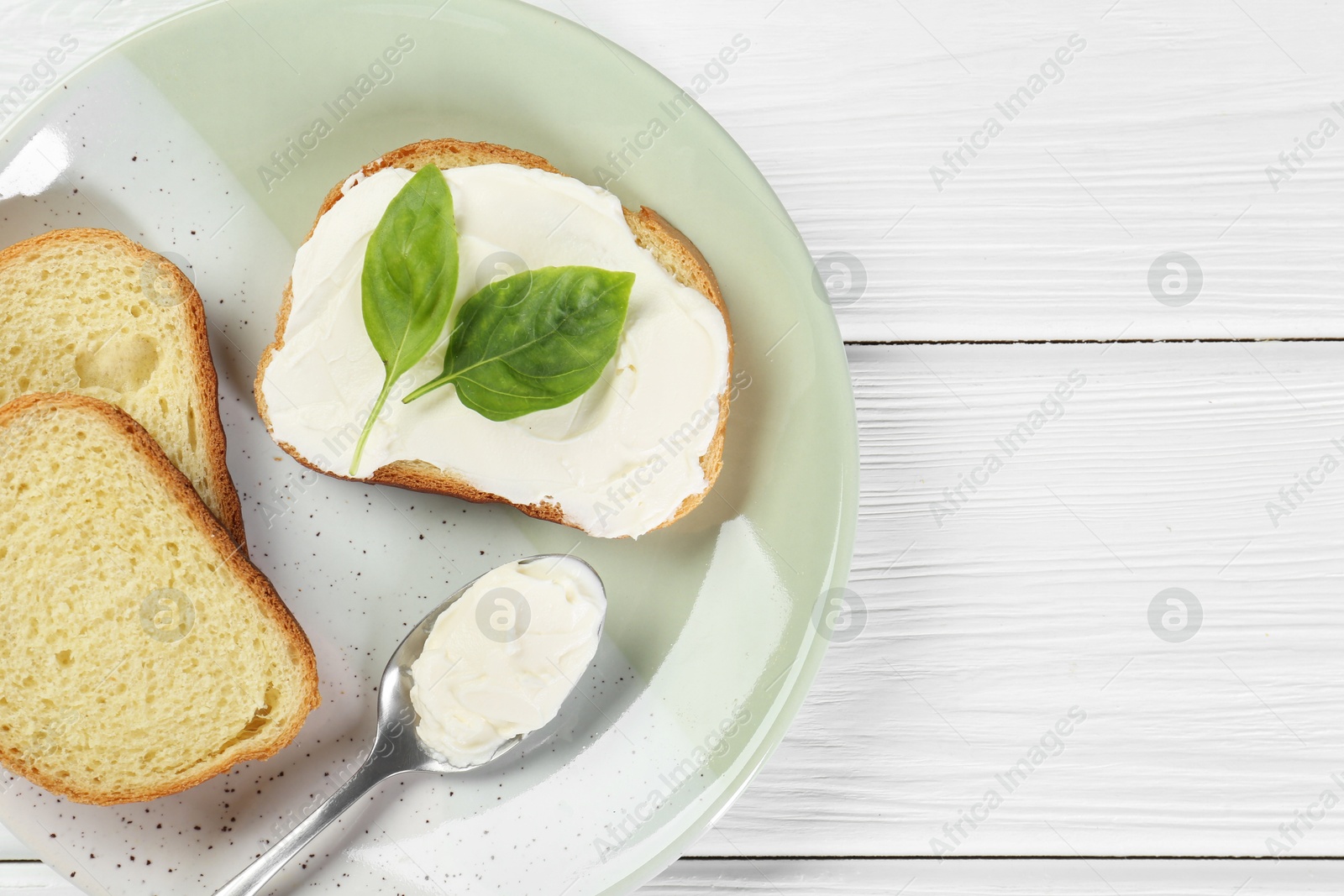 Photo of Pieces of bread with cream cheese and basil leaves on white wooden table, top view. Space for text