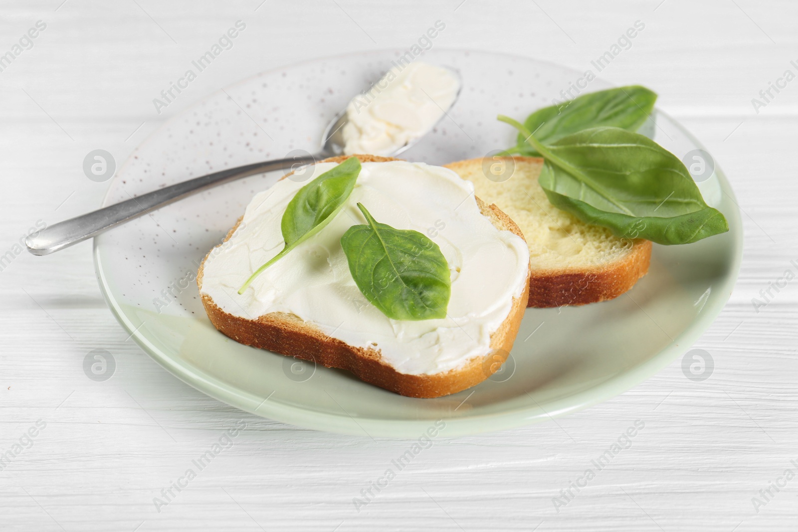 Photo of Pieces of bread with cream cheese and basil leaves on white wooden table