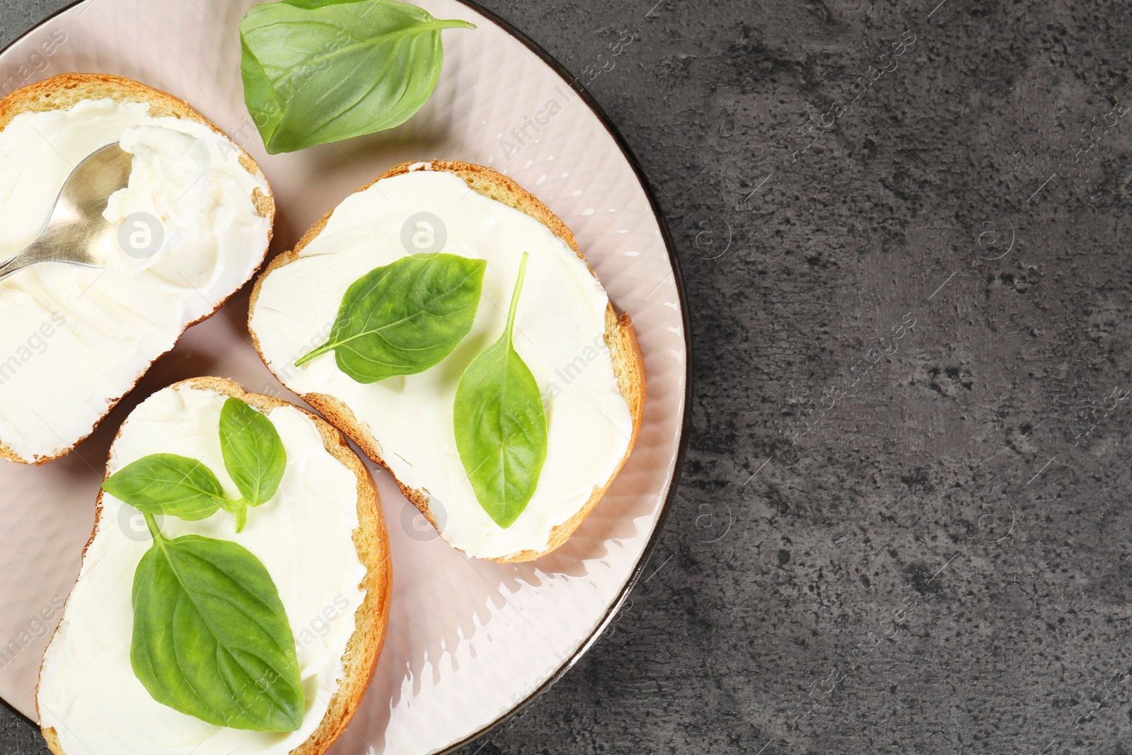 Photo of Delicious sandwiches with cream cheese and basil leaves on grey table, top view. Space for text