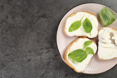 Delicious sandwiches with cream cheese and basil leaves on grey table, top view. Space for text