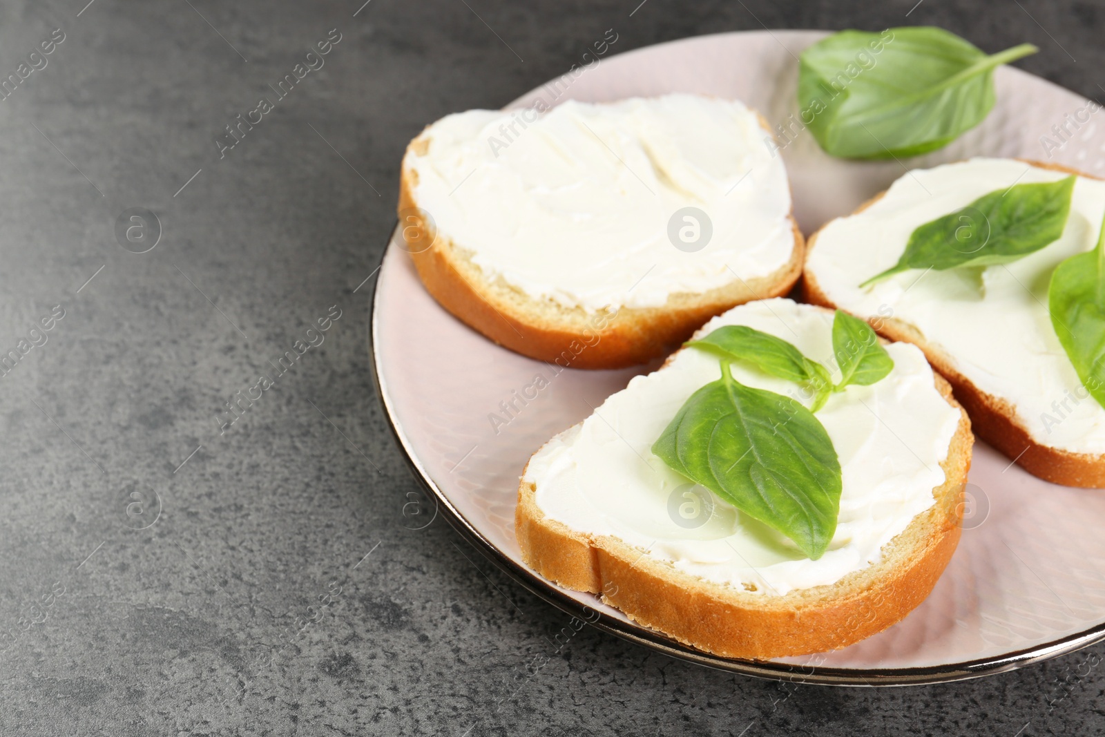 Photo of Delicious sandwiches with cream cheese and basil leaves on grey table, closeup. Space for text