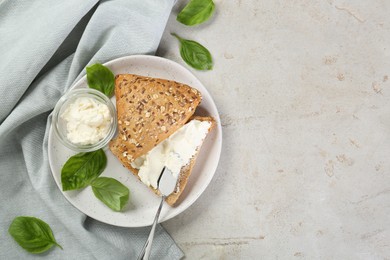 Pieces of bread with cream cheese and basil leaves on light gray textured table, top view. Space for text