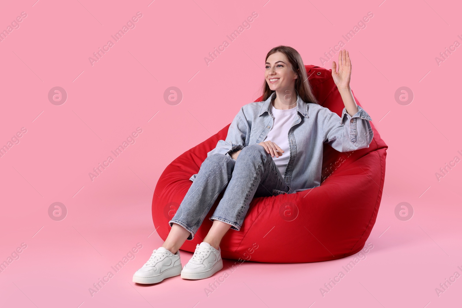 Photo of Smiling woman sitting on red bean bag chair against pink background, space for text