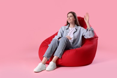Photo of Smiling woman sitting on red bean bag chair against pink background, space for text