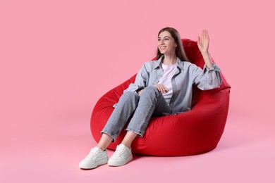 Smiling woman sitting on red bean bag chair against pink background, space for text