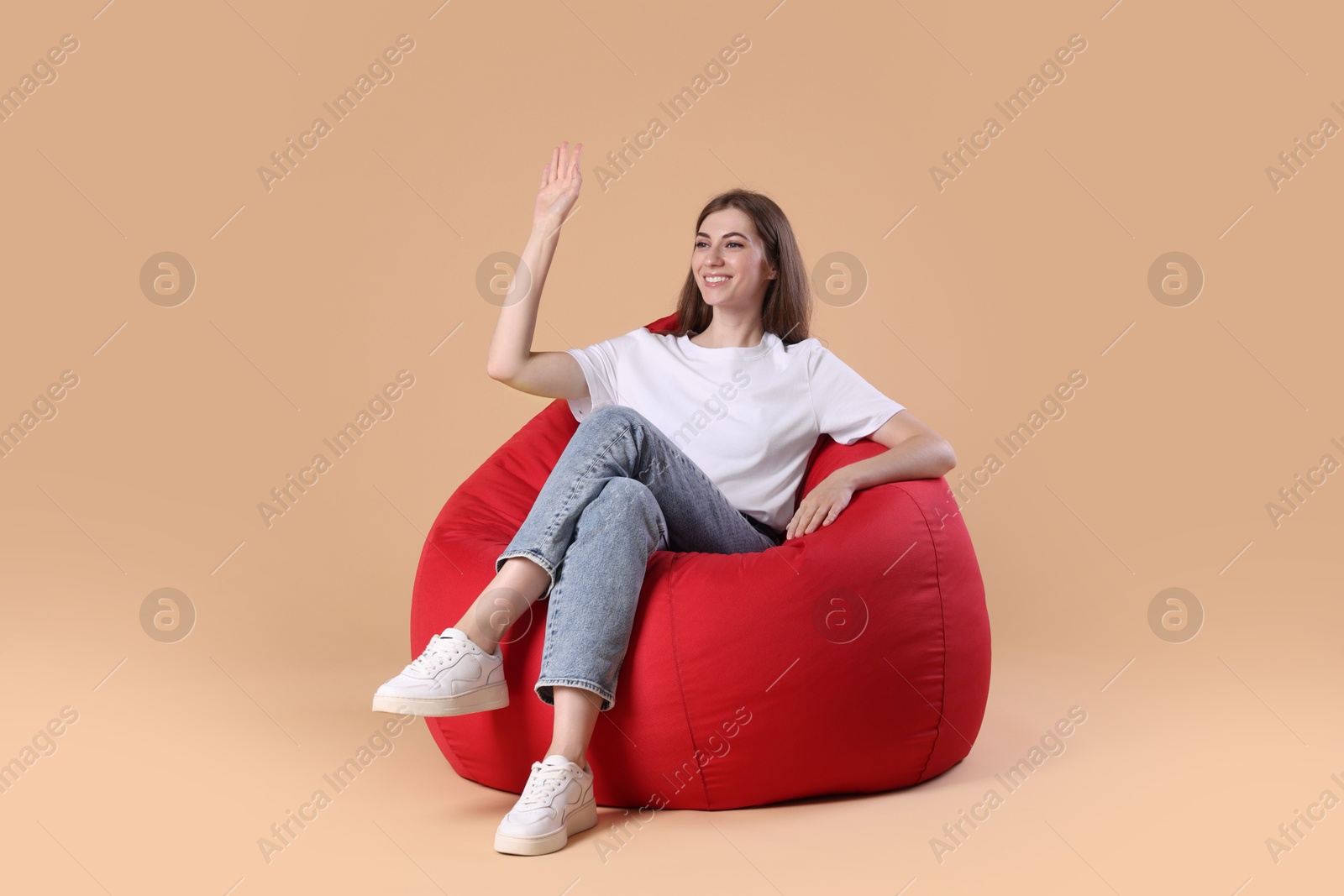 Photo of Smiling woman on red bean bag chair against beige background