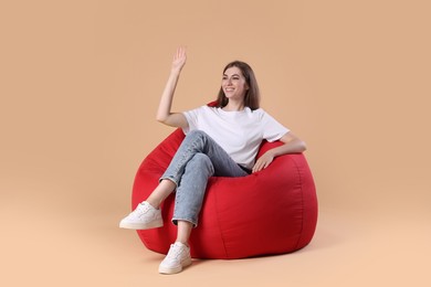 Smiling woman on red bean bag chair against beige background