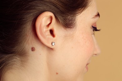 Woman with mole on her skin against beige background, closeup