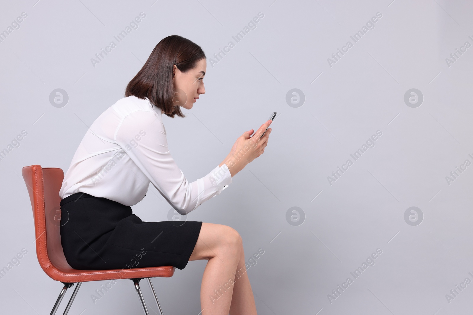 Photo of Woman with poor posture sitting on chair and using smartphone against gray background, space for text