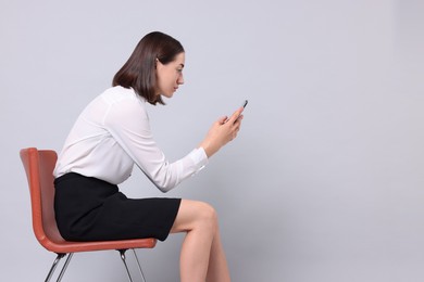 Photo of Woman with poor posture sitting on chair and using smartphone against gray background, space for text