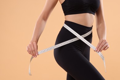 Photo of Diet and weight loss concept. Woman with measuring tape showing her slim body against beige background, closeup