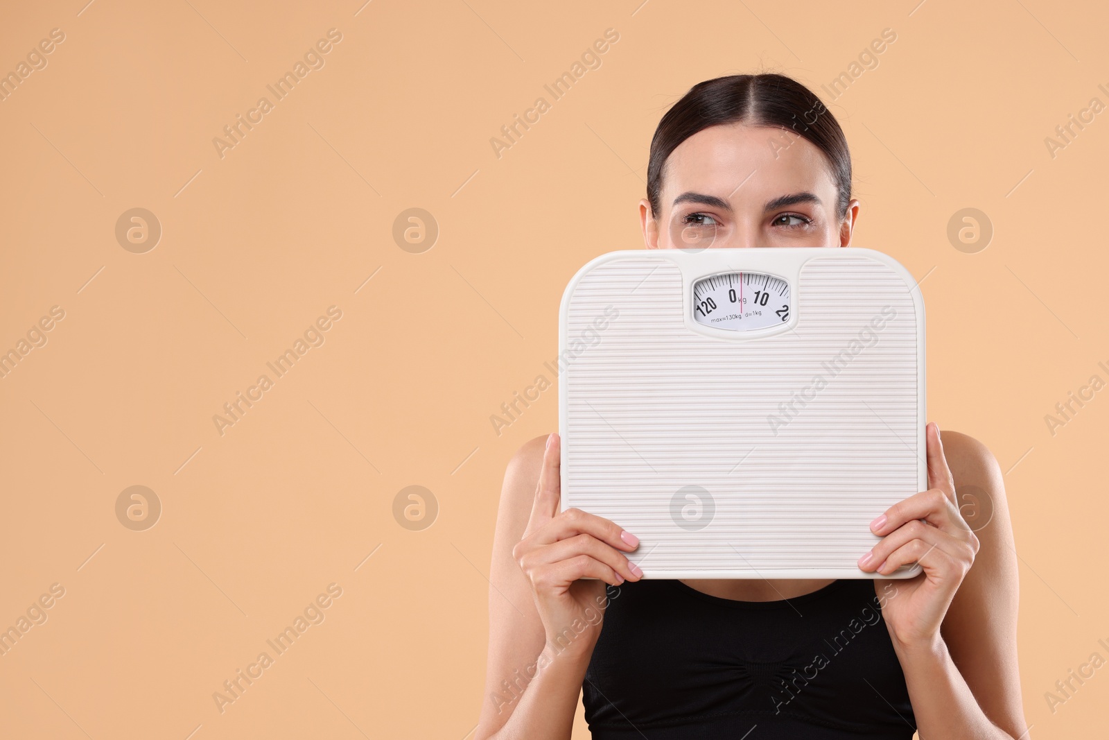 Photo of Diet and weight loss concept. Young woman with floor scale on beige background. Space for text