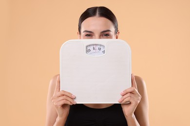 Photo of Diet and weight loss concept. Young woman with floor scale on beige background