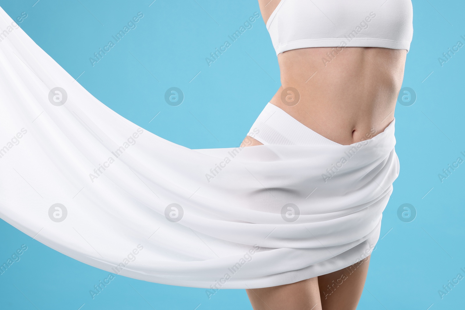 Photo of Diet and weight loss concept. Woman covering her slim body with silk fabric against light blue background, closeup