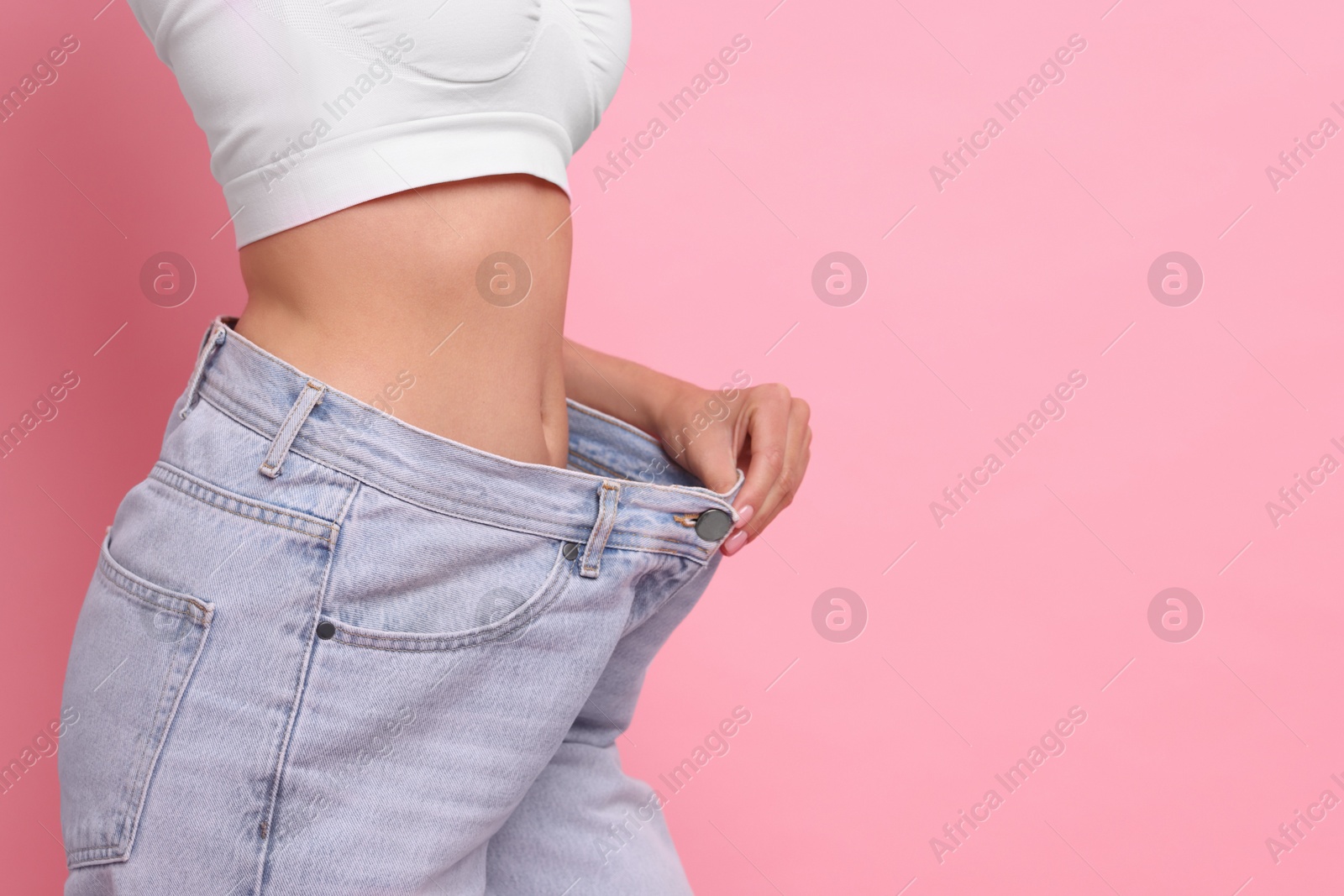 Photo of Diet and weight loss concept. Woman in big jeans showing her slim body on pink background, closeup. Space for text