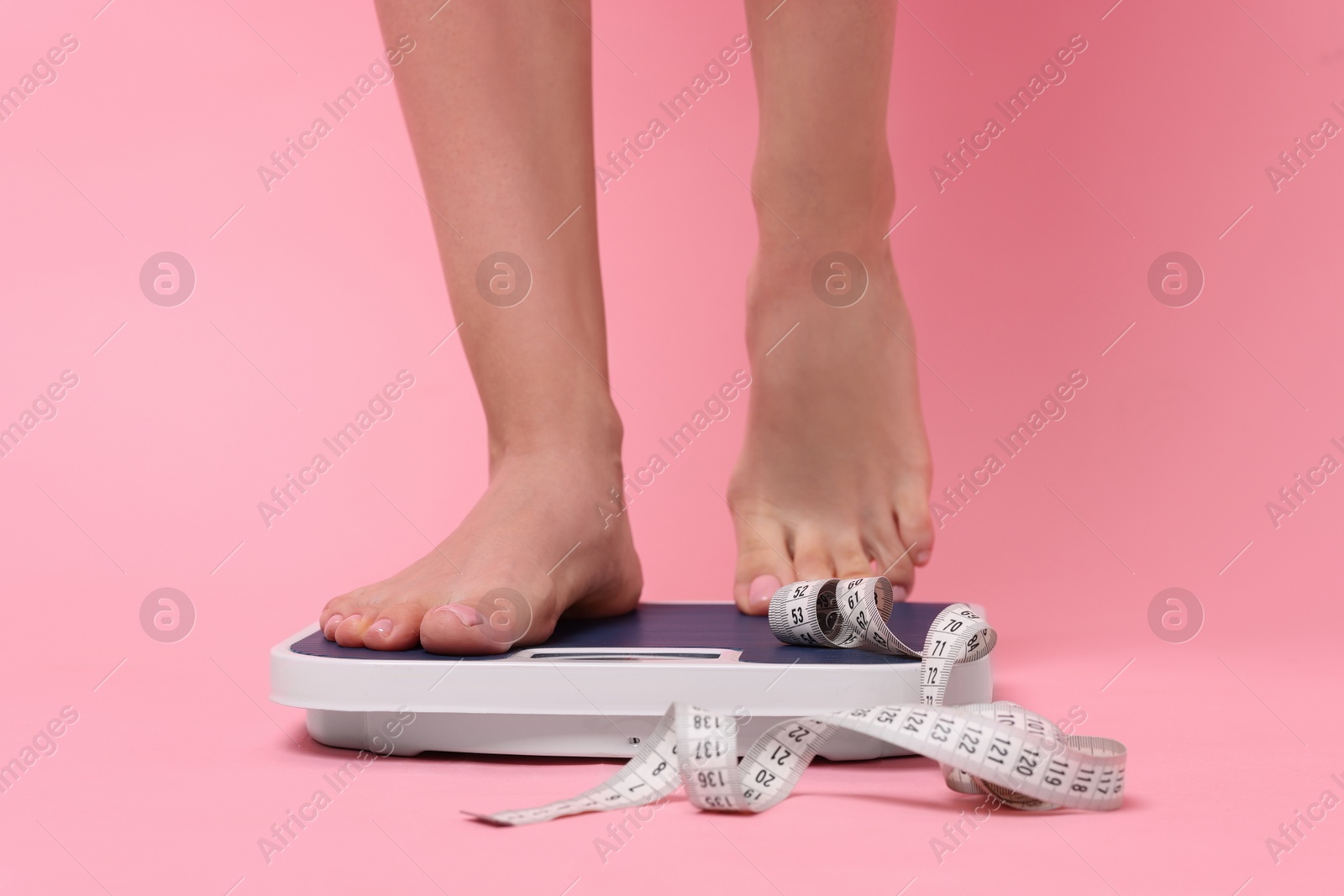 Photo of Diet and weight loss concept. Woman on floor scale and measuring tape against pink background, closeup