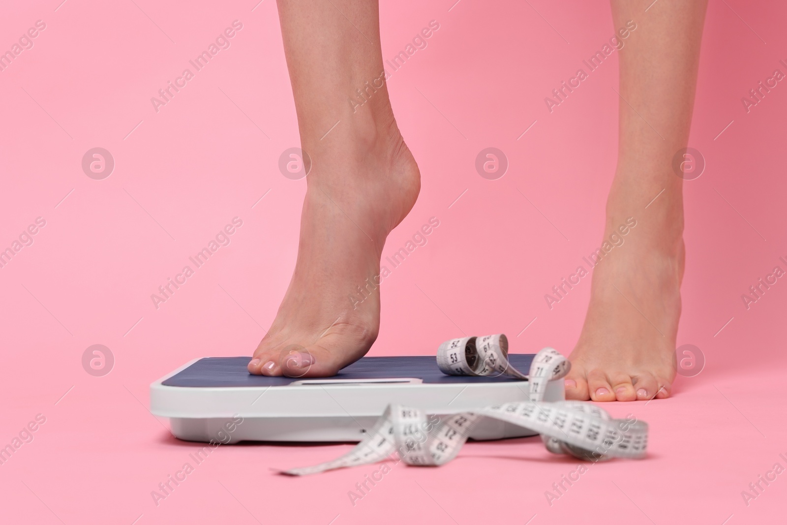 Photo of Diet and weight loss concept. Woman on floor scale and measuring tape against pink background, closeup