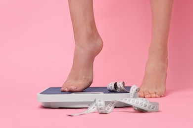 Photo of Diet and weight loss concept. Woman on floor scale and measuring tape against pink background, closeup