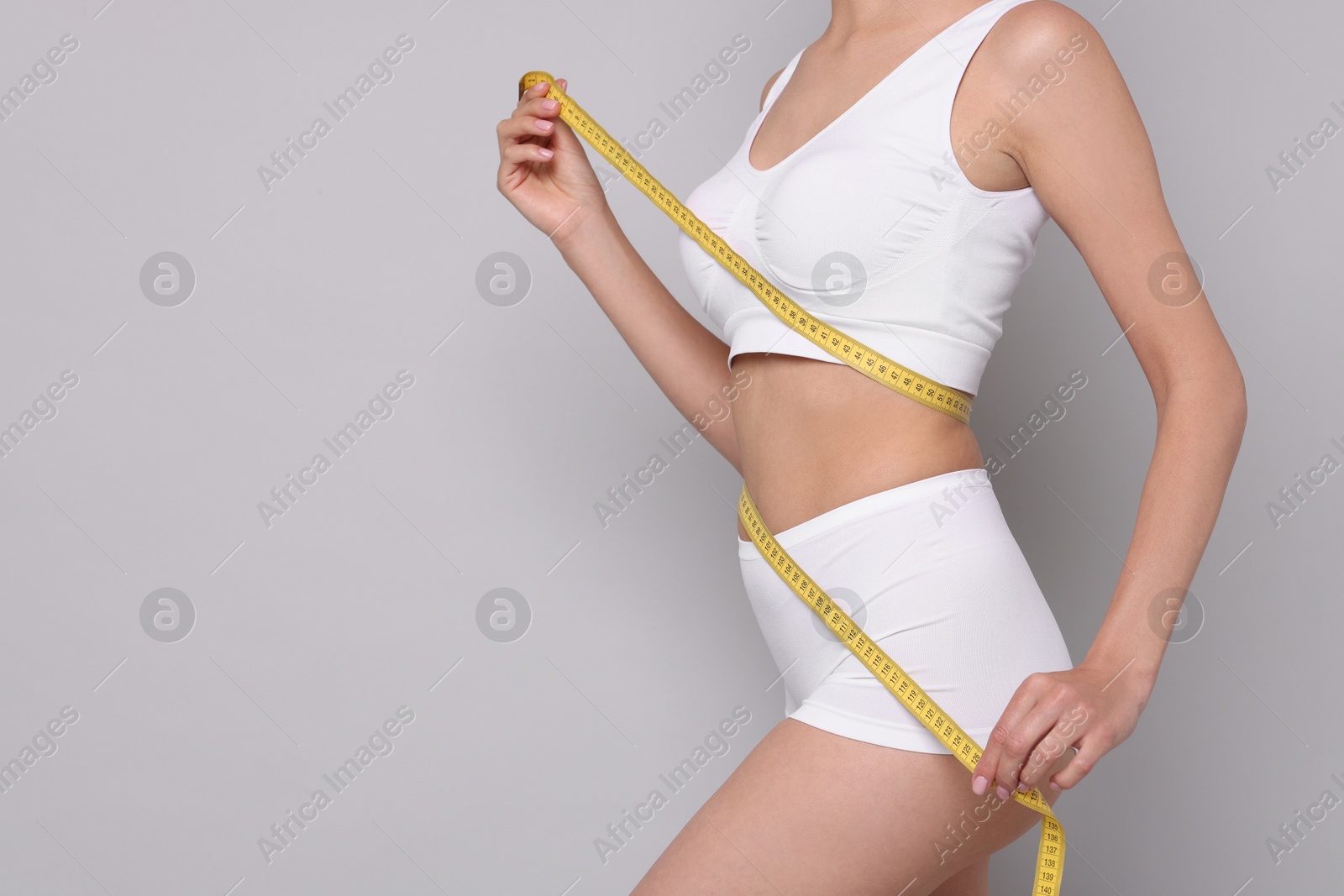 Photo of Diet and weight loss concept. Woman with measuring tape showing her slim body against light grey background, closeup. Space for text