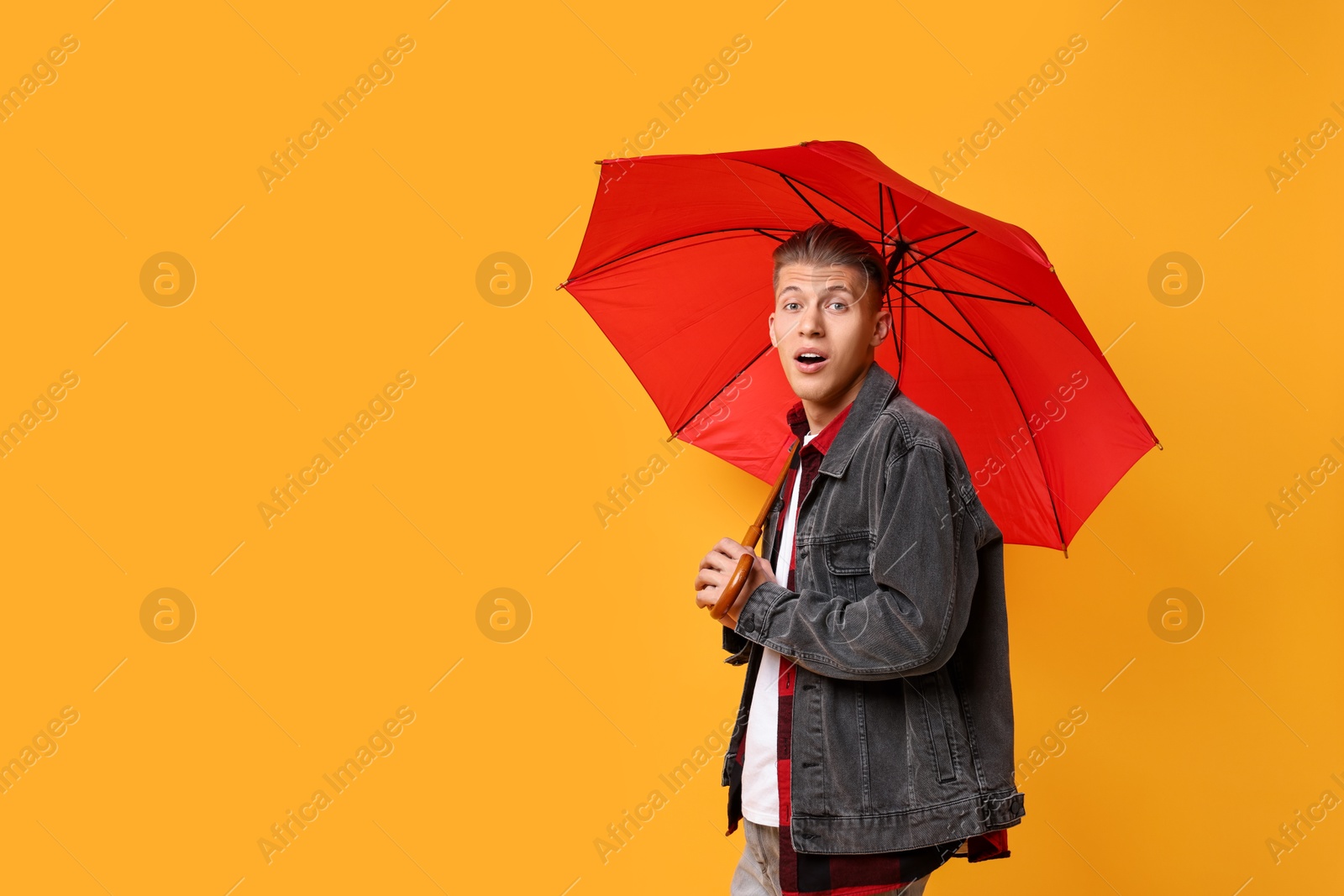 Photo of Young man with red umbrella on yellow background, space for text