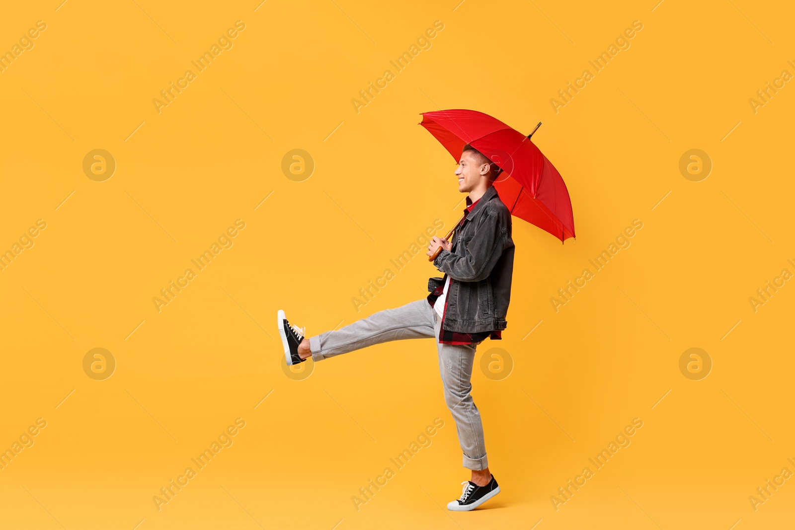 Photo of Young man with red umbrella on yellow background, space for text