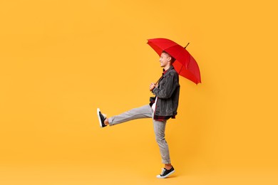 Photo of Young man with red umbrella on yellow background, space for text