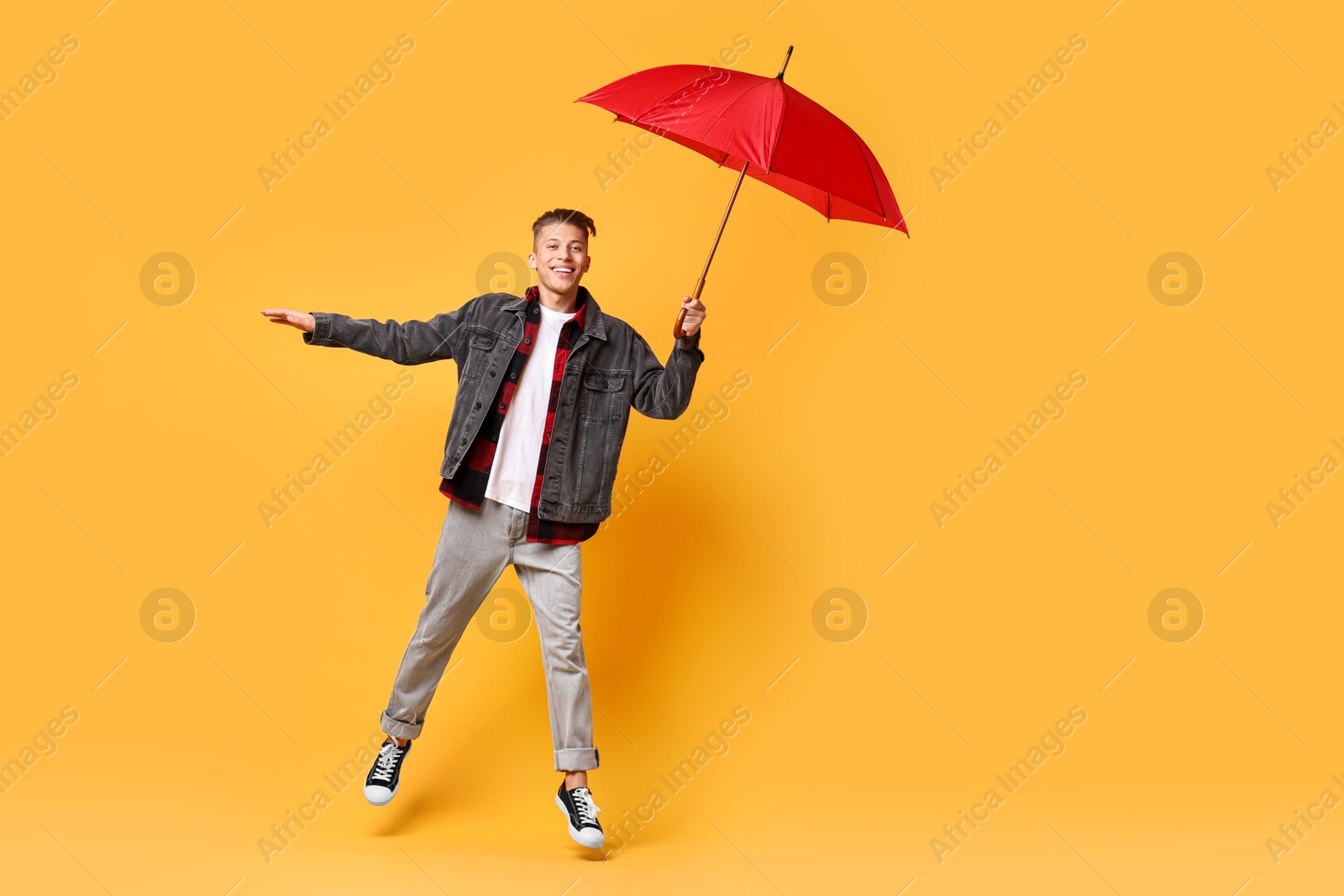 Photo of Young man with red umbrella jumping on yellow background, space for text