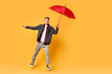 Photo of Young man with red umbrella jumping on yellow background, space for text
