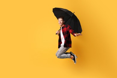 Photo of Young man with black umbrella jumping on yellow background, space for text