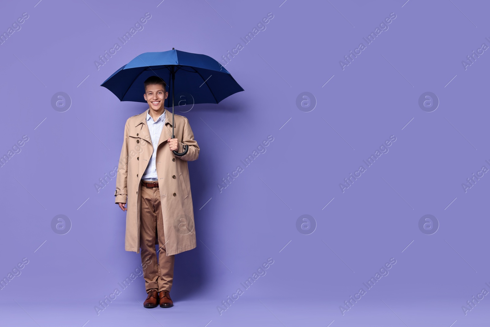 Photo of Young man with blue umbrella on purple background, space for text