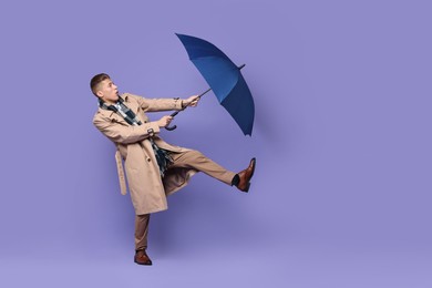 Photo of Young man with blue umbrella on purple background, space for text