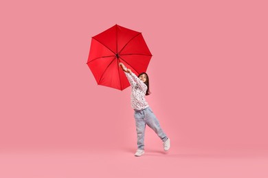 Cute little girl with red umbrella on pink background