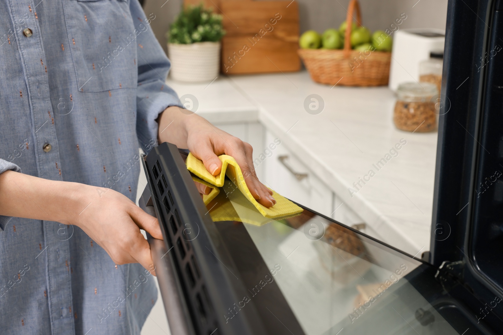 Photo of Woman cleaning oven door with rag in kitchen, closeup